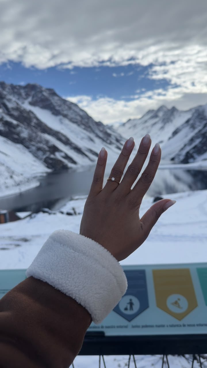 Mão com anel de noivado diante de montanhas com neve